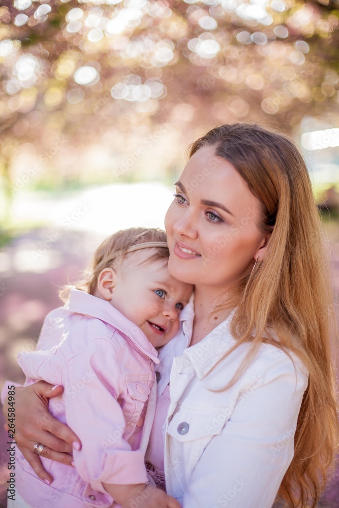 Beautiful young mother and little cute daughter are happy walking in a flowered park. Portrait of mom and daughter. Cherry blossoms. Beautiful young mother and little cute daughter are happy walking in a flowered park. Portrait of mom and daughter. Cherry blossoms.