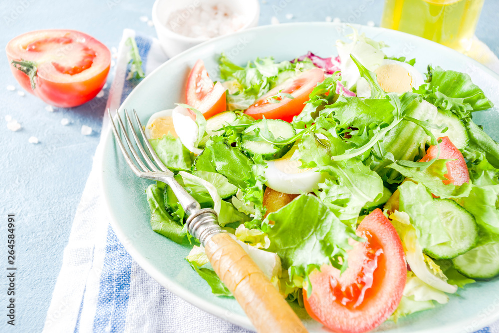 Spring healthy diet salad with leaf vegetables, cucumber, tomatoes, eggs, with olive oil, blue concrete background copy space Spring healthy diet salad with leaf vegetables, cucumber, tomatoes, eggs, with olive oil, blue concrete background copy space