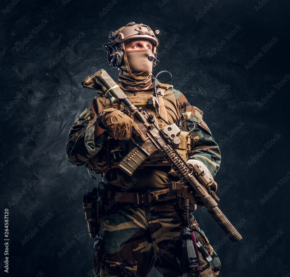 Fototapeta premium Elite unit, special forces soldier in camouflage uniform posing with assault rifle. Studio photo against a dark textured wall