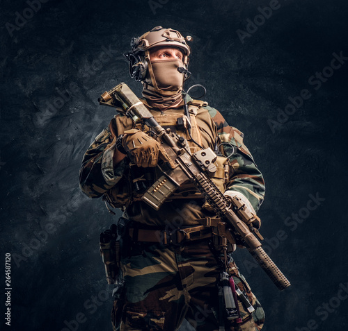 Elite unit  special forces soldier in camouflage uniform posing with assault rifle. Studio photo against a dark textured wall