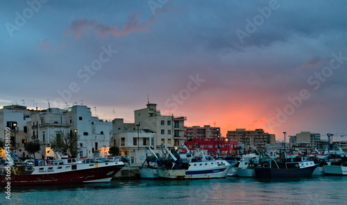 Monopoli, Puglia, Italy - April 07, 2019: sunset on the old town harbor with fishing ships and vessels in the internal dock