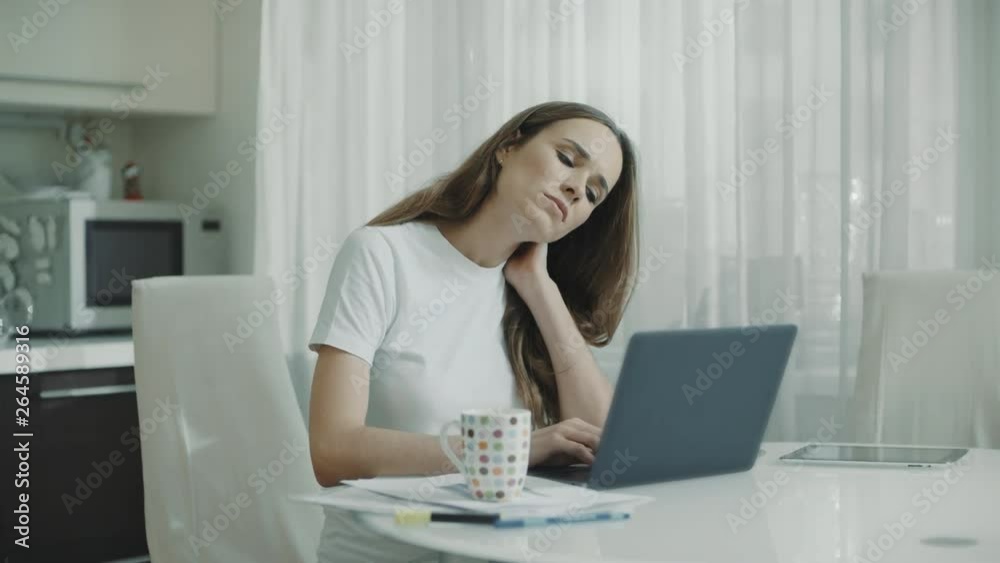 Tired woman working on laptop computer at home. Stressed woman touching neck Tired woman working on laptop computer at home. Stressed woman touching neck