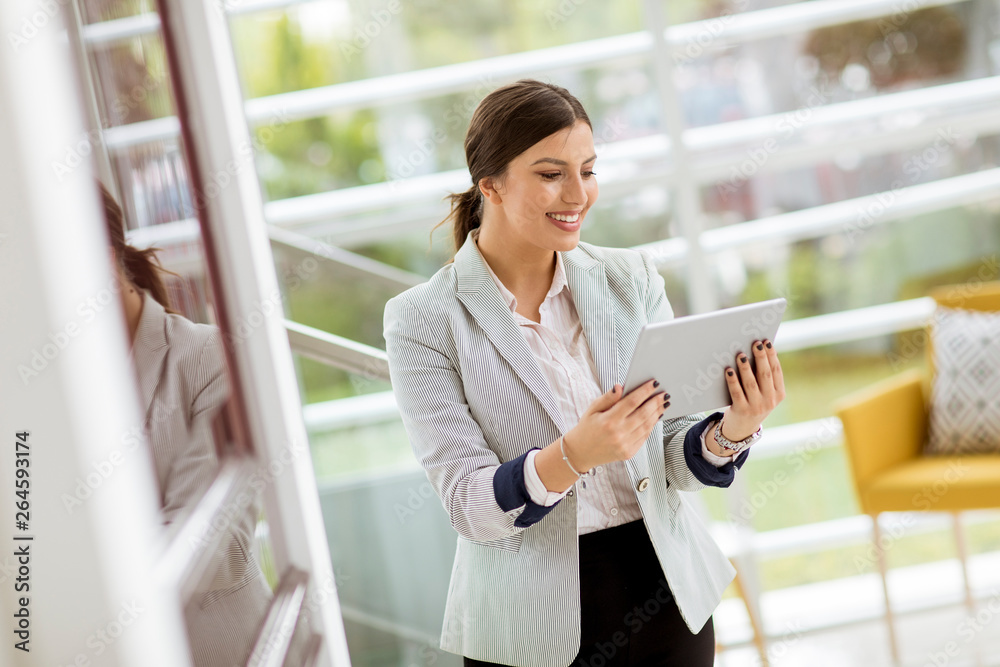 Portrait of attractive young business woman smiling confidently and working online with a digital tablet while standing in a modern office