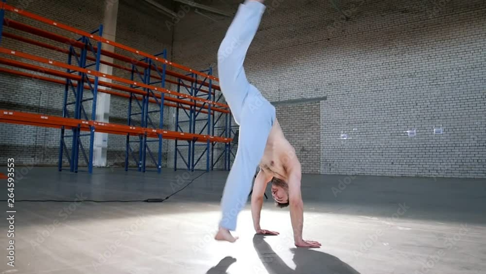 A bright room. An athletic man training his capoeira skills and performing flips A bright room. An athletic man training his capoeira skills and performing flips