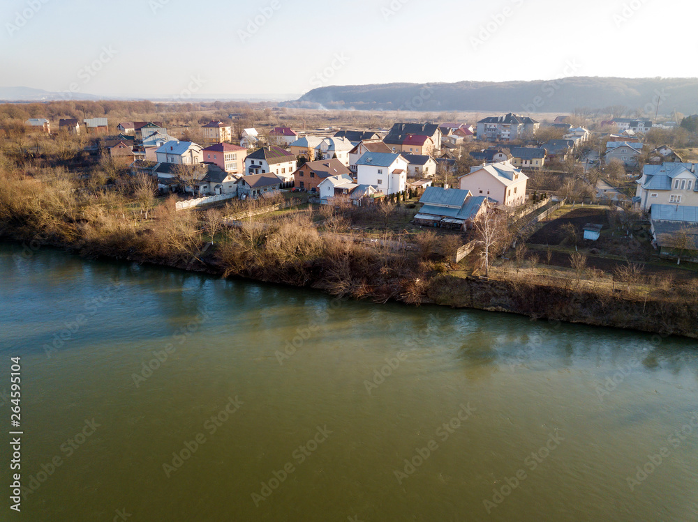 Aerial top view, countryside panorama of residential houses on river bank on blue sky and woody hill background. Drone photography.