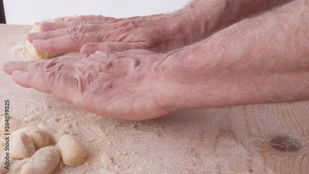 Mani di un uomo stanno preparando e impastando gli gnocchi di patate. Con farina integrale e uova fatti in in casa, su un tagliere di legno.