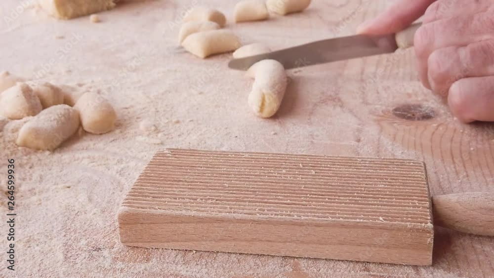 Mani di un uomo stanno preparando e impastando gli gnocchi di patate. Con farina integrale e uova fatti in in casa, su un tagliere di legno. Rigatura con rigagnocchi.