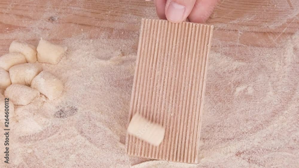 Mani di un uomo stanno preparando e impastando gli gnocchi di patate. Con farina integrale e uova fatti in in casa, su un tagliere di legno. Fase della rigatura con rigagnocchi.