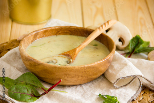 Mushroom soup with champignons. Paleo diet, chicken broth soup with mushrooms and cheese. Soup in a wooden bowl with a wooden spoon. Background about lunch. Copy space