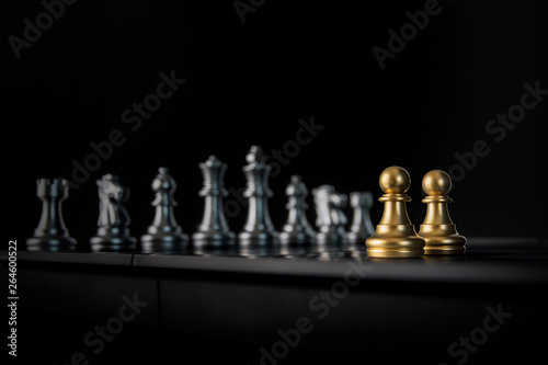 Two golden chess pawns are facing silver chess on black background. Business partnership concept.
