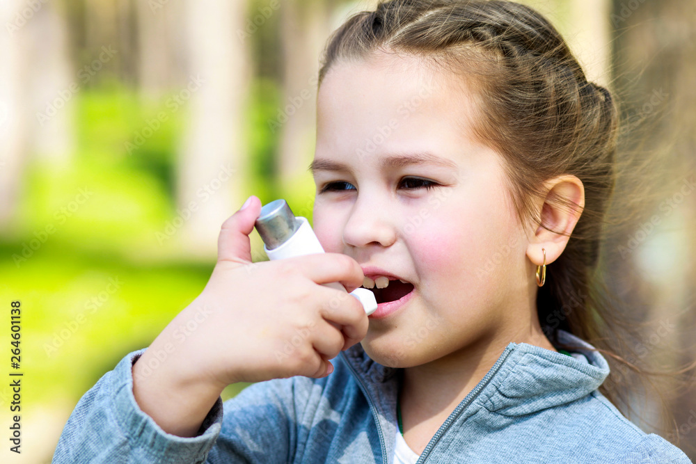 Asian small child using an inhaler during an asthma attack in the park Asian small child using an inhaler during an asthma attack in the park