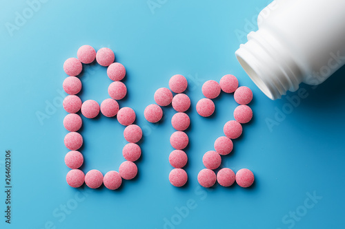 Wallpaper Mural Pink pills in the shape of the letter B12 on a blue background, spilled out of a white can. Torontodigital.ca