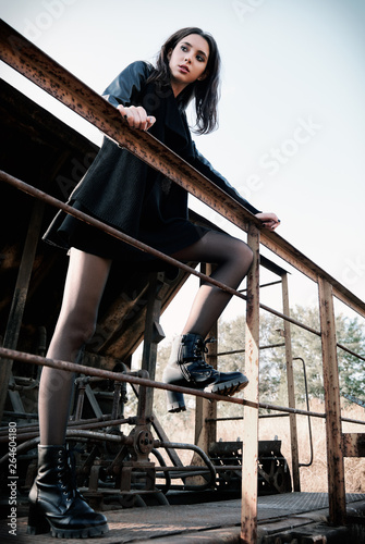 Fashion shot: portrait of pretty rock girl (informal model) dressed in black jacket and skirt standing on train car