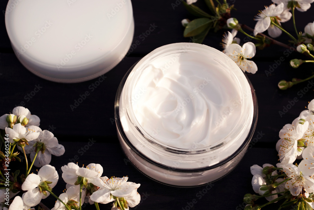 Eco cream in round tuba on black ooden background with white flowers. View from above. Eco cream in round tuba on black ooden background with white flowers. View from above.