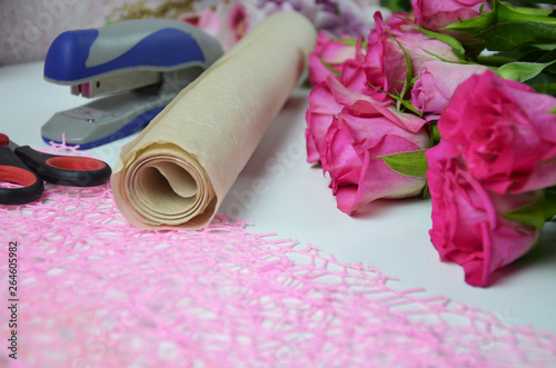 Florist at work: pretty woman making summer bouquet of roses on a working table. Kraft paper, scissors, envelope for congratulations on the table. View from above. Flat lay composition. photo