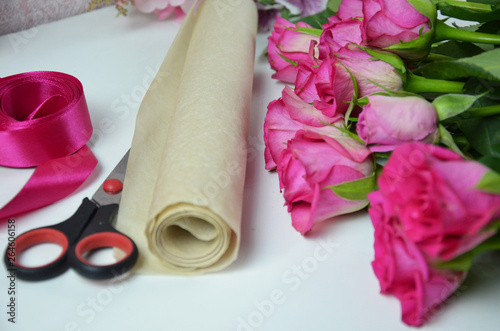 Florist at work: pretty woman making summer bouquet of roses on a working table. Kraft paper, scissors, envelope for congratulations on the table. View from above. Flat lay composition. © Dilya