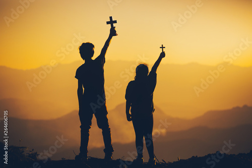 Two people standing holding christian cross for worshipping God at sunset background. christian silhouette concept.