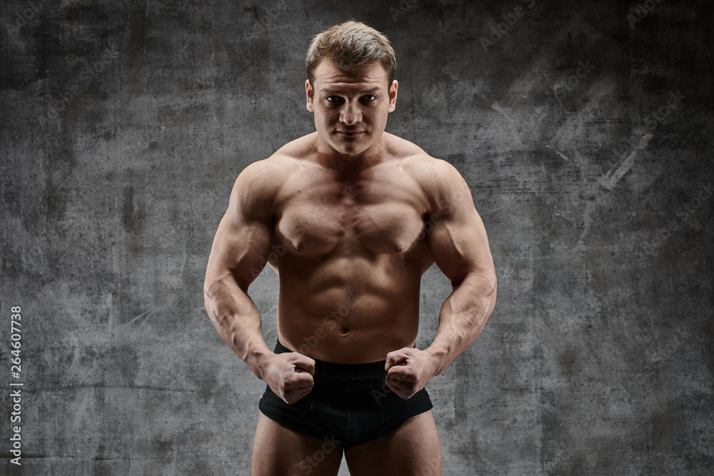 Sexy bodybuilder man posing on dark background in black shorts. Handsome pumped male body isolated with free space for advertising