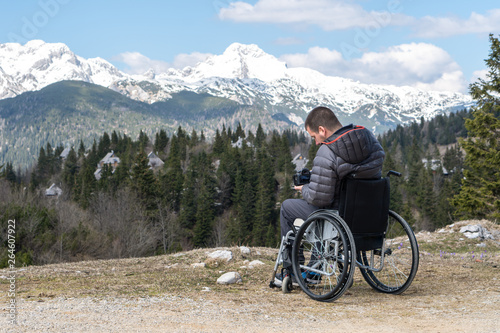 Disabled man on wheelchair using camera in nature, photographing beautiful mountains