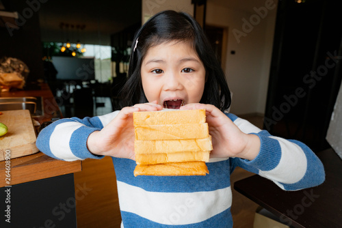 asian healthy kid girl in blue and white sweater enjoy and feel good with bread sandwish in kitchen photo