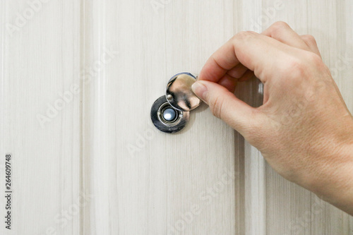 Fotografija The hand opens the door peephole cover in the front door of light oak