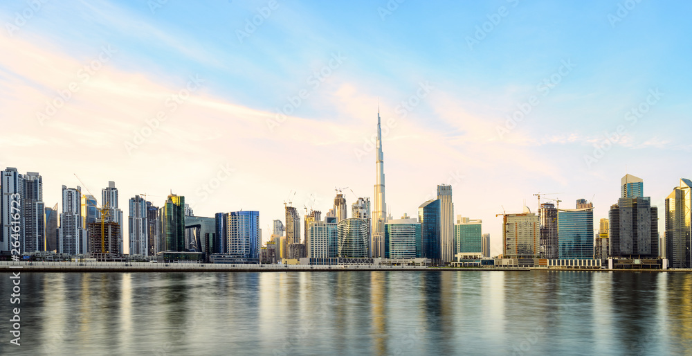 Stunning panoramic view of the Dubai skyline during sunset with the magnificent Burj Khalifa and many other buildings and skyscrapers reflected on a silky smooth water. Dubai, United Arab Emirates.