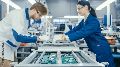 Shot of an Electronics Factory Workers Assembling Circuit Boards by Hand While it Stands on the Assembly Line. High Tech Factory Facility.