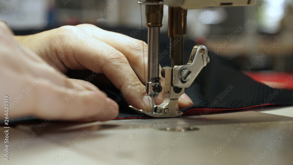 A seamstress in a seamstress factory (at home) sews clothes from fabric materials. Using a sewing machine in slow motion. Concept of: Factory, Work, Labor, Cloth, People, Macro, Clothes. Stock Photo |