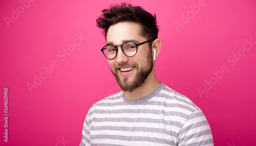 Photo of smiling man wearing glasses, and aipods, lookinf at camera over pink background photo