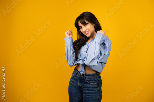 Young beautiful girl in a blue shirt posing for a photo on a yellow background.