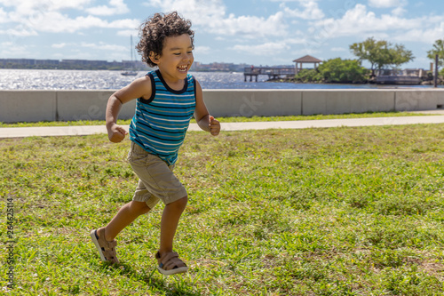 A young boy runs across the field while laughing out loud. The happy toddler is having a wonderful time running outdoors at the waterfront park. photo