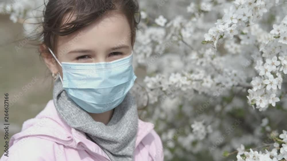 A child in a medical mask in the spring. Little girl in a protective mask during spring flowering. Allergy to pollen. A child in a medical mask in the spring. Little girl in a protective mask during spring flowering. Allergy to pollen.