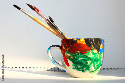 Art paint brushes in a cup with empty space for text on a white sketchbook background. Creative album for drawing, Art school concept, hobbies, creativity groups for kids education. Copy space.