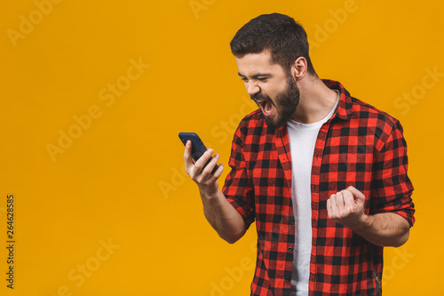 Angry young man screaming on the cell phone isolated on a yellow background. © denis_vermenko