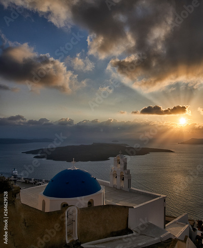 Sunset with sunrays shining between clouds over little church on the Greek island of Santorini