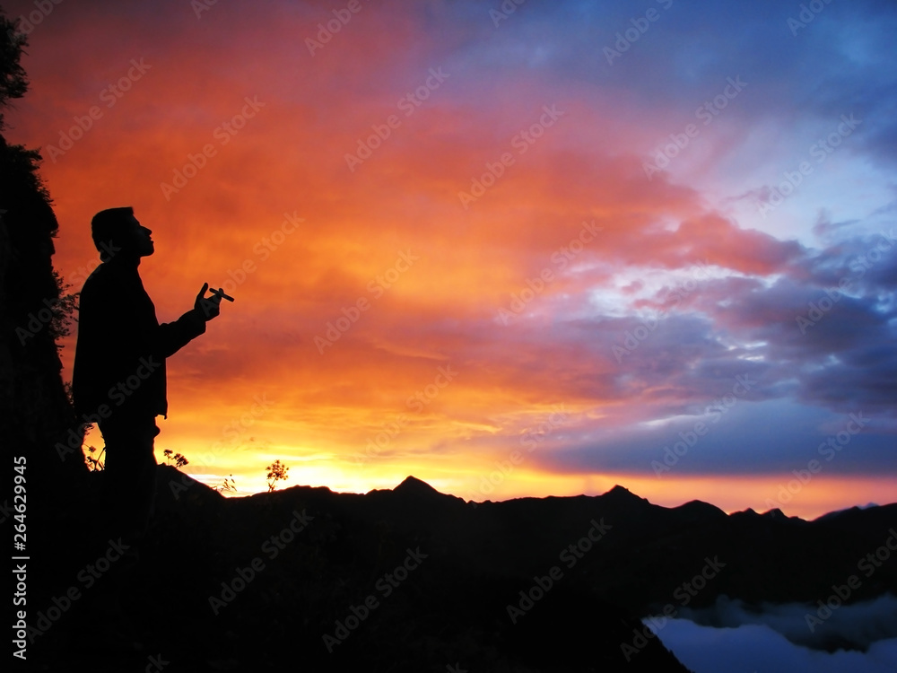 Black silhouette of a man smoking a cigar against the background of a bright contrasting sunset in the mountains in the Alps.