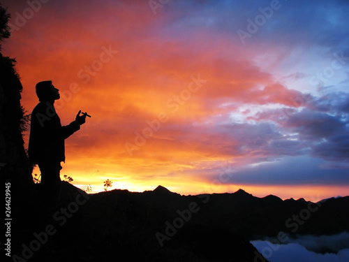 Black silhouette of a man smoking a cigar against the background of a bright contrasting sunset in the mountains in the Alps.