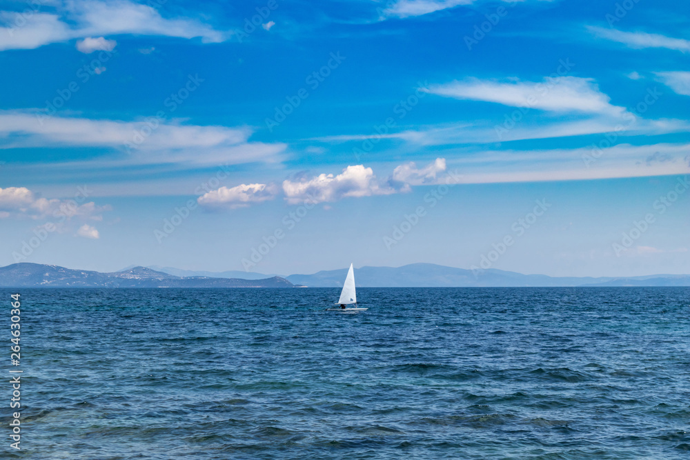 Small optimist boat with white sail, blue sky and sea background Small optimist boat with white sail, blue sky and sea background