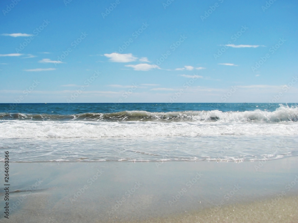 Fototapeta premium Waves tide near the shore on a sandy beach and blue sky.