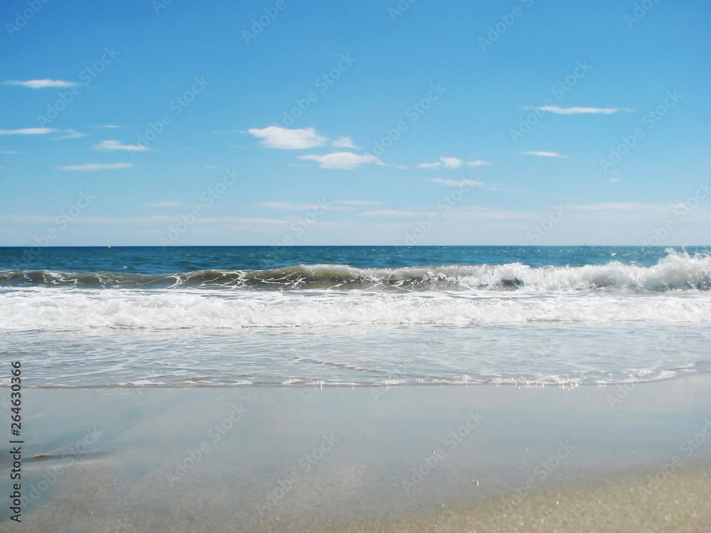 Waves tide near the shore on a sandy beach and blue sky.