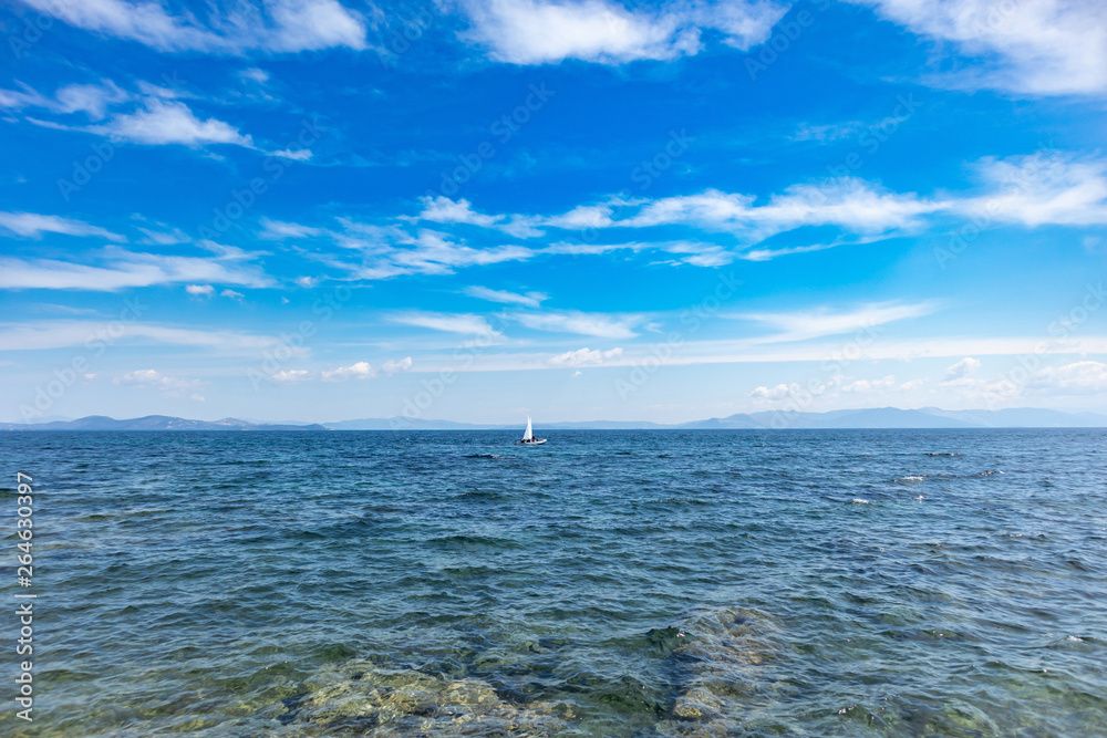 Small optimist boat with white sail, blue sky and sea background