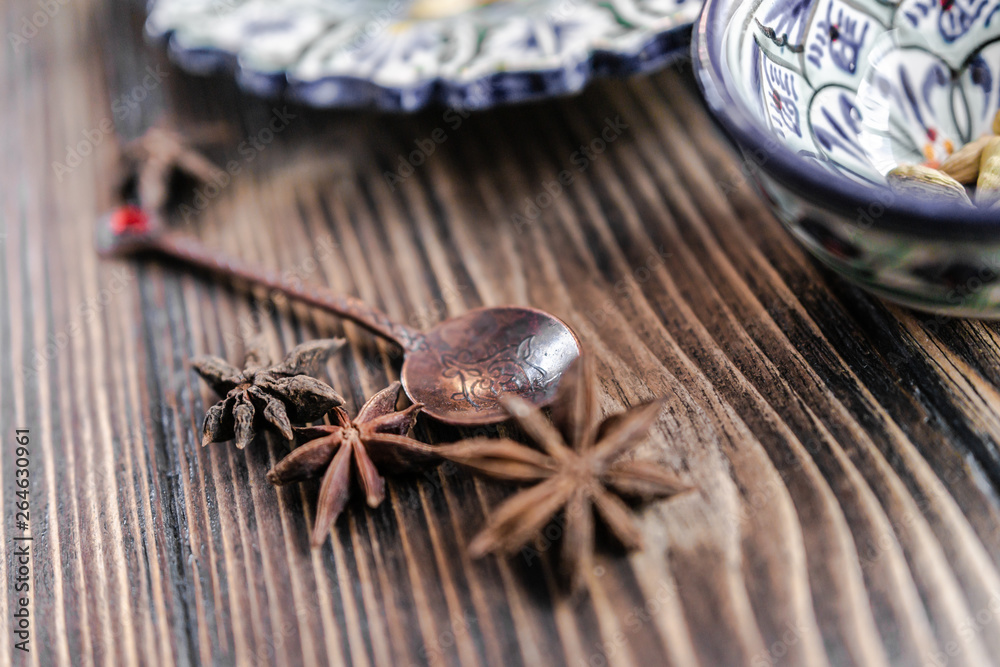 Authentic middle east style bronze spoon with a cinnamon on the wooden desk with a colourful eastern bowl and a plate on the black background. Isolated. Shallow depth of field. Horizontal orientation. Authentic middle east style bronze spoon with a cinnamon on the wooden desk with a colourful eastern bowl and a plate on the black background. Isolated. Shallow depth of field. Horizontal orientation.