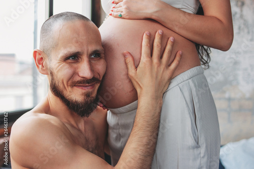 Happy future father listening to baby belly of his wife. Authentic couple, family waiting for baby