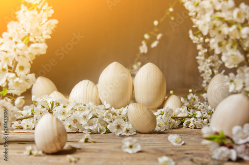 wooden easter eggs among flowering cherry branches on a rustic table. symbolic composition of the spring holiday for a gift card. copy space. close up. petals of white flowers. the rebirth of nature