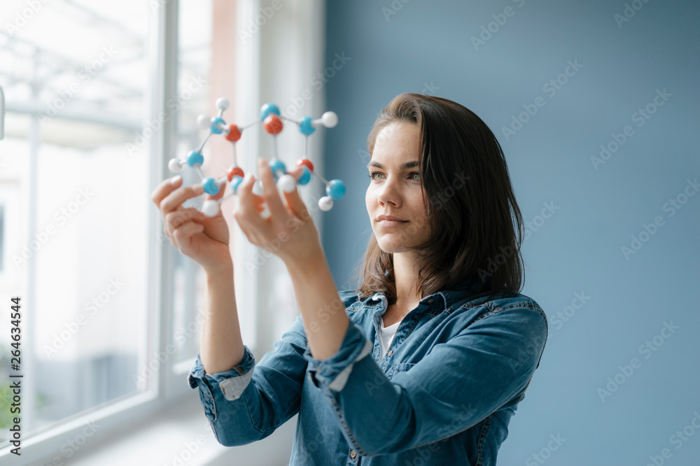 Female scientist studying molecule model, looking for solutions