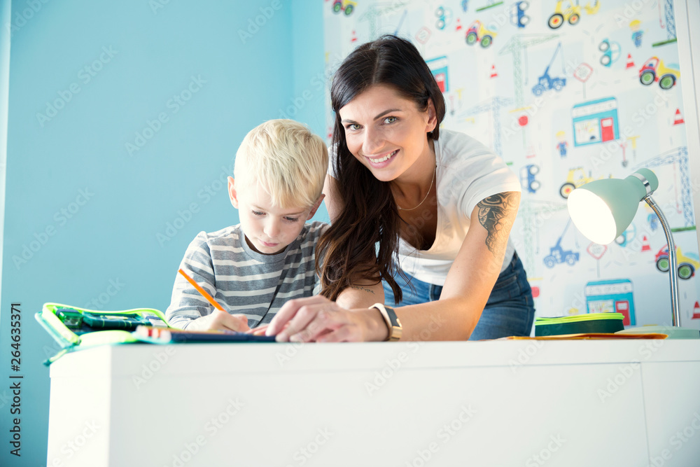 Portrait of smiling mother helping son doing homework at desk Portrait of smiling mother helping son doing homework at desk
