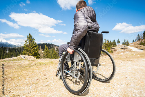 Wide angle photo ofYoung disabled man in wheelchair outside in nature observing mountains and nature photo