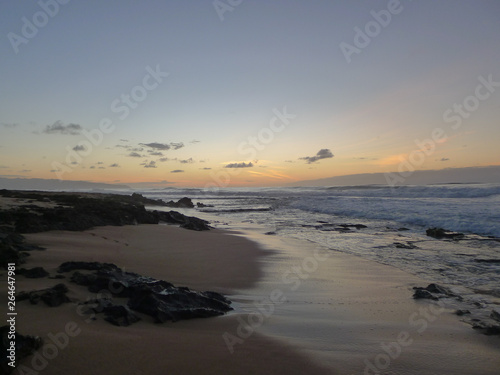 Beach at the North Shore on Oahu, Hawaii with surfing waves and a dark rocks in the sand. Sun recently went down.
