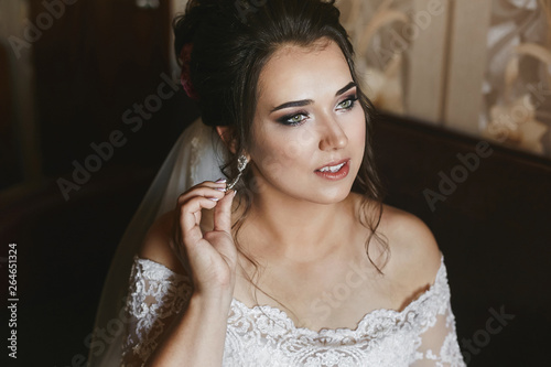 Beautiful model plus size in a fashionable wedding dress and with stylish wedding hairstyle adjusting her earring before the wedding ceremony