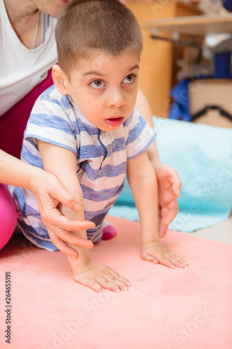 little kid with cerebral palsy has musculoskeletal therapy by doing exercises in body fixing. Load on hands,cheerful boy with disability at rehabilitation center for kids with special needs